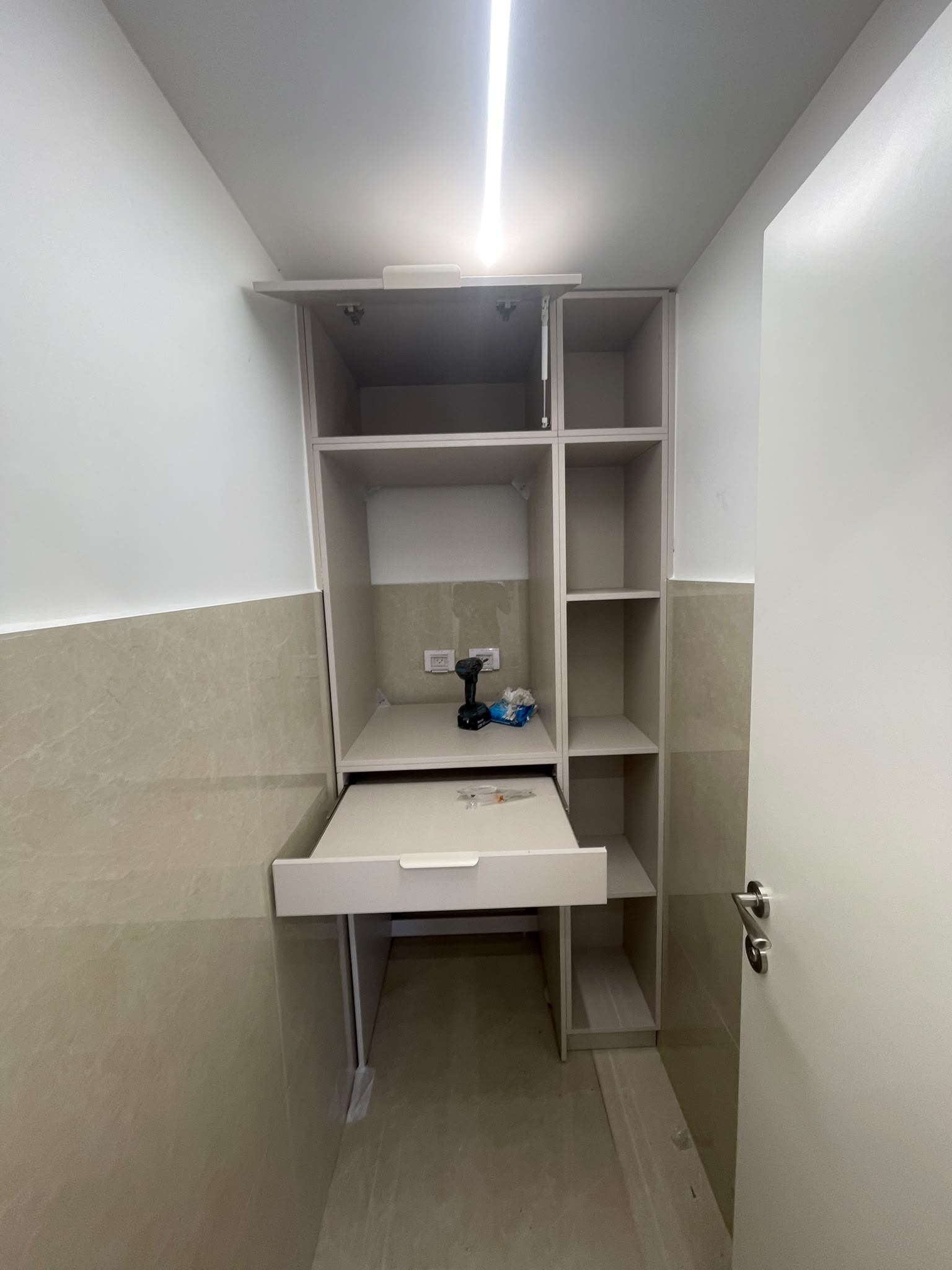 יחידת שירות דגם נישה — יחידה גבוהה עם משטח קיפול נשלף, תא סגור למכונה ומדפים פתוחים — בשלב ההרכבה בנגרייה.