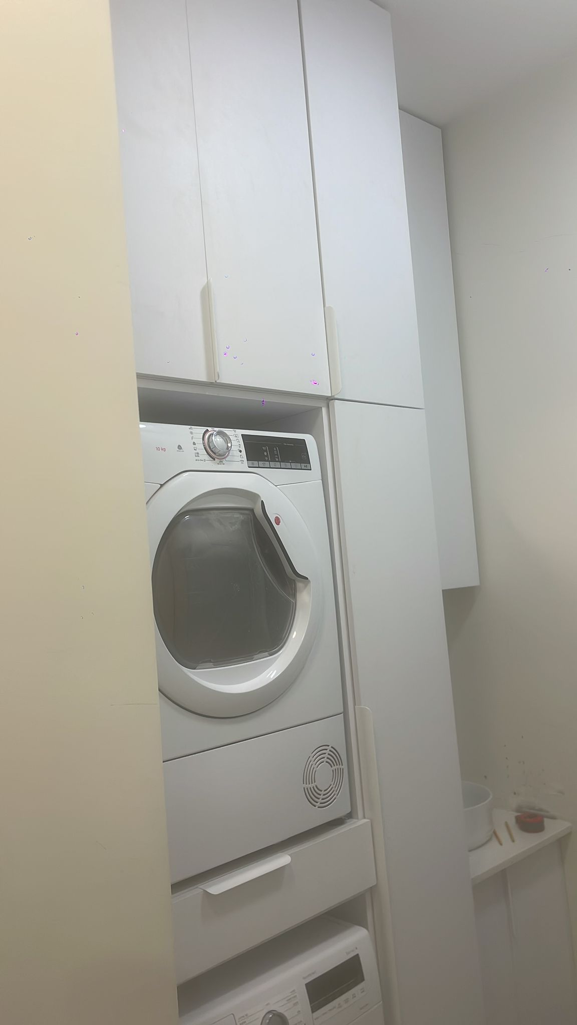 עמדת כביסה דגם עמודה — עמודה צרה וגבוהה עם מכונות בקומותיים, ארונות עליונים ומגירה תחתונה.